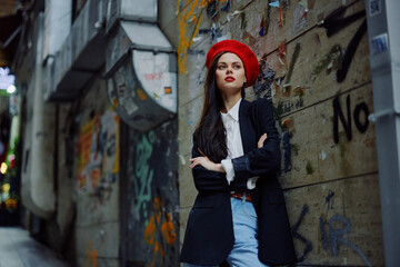 Naklejka premium Fashion woman portrait walking tourist in stylish clothes with red lips walking down a narrow city street, travel, cinematic color, retro vintage style, dramatic against a wall with graffiti.