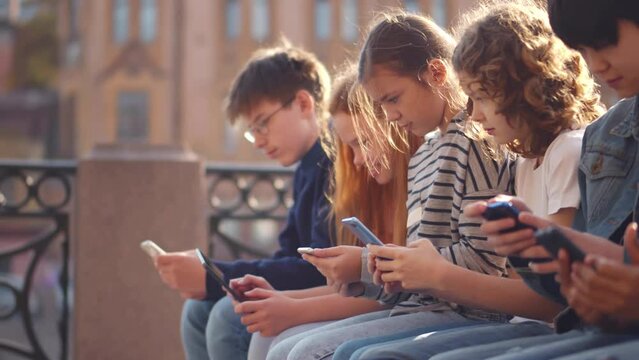 Multiethnic group of school students outdoors use mobile phones. Realtime