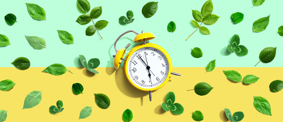 Yellow vintage alarm clock with green leaves - flat lay - obrazy, fototapety, plakaty