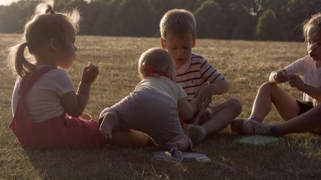 people in the park. happy family silhouette sitting on grass at sunset. mom with three kids eating fruits Grapes snack picnic time. children playing spend time outside. parents Friendship Siblings