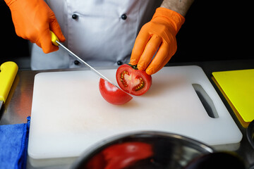 chef in orange gloves cuts a tomato on a cutting board