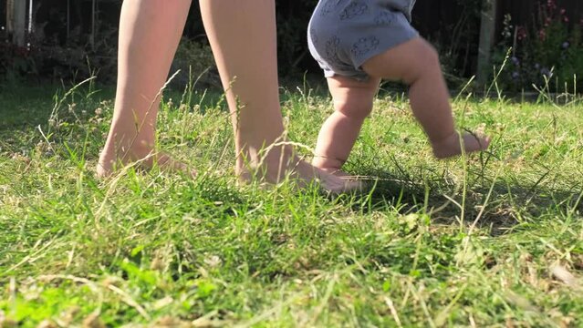 baby takes first steps in grass. mom walks with son in nature kid dream concept. baby takes first steps with mom. mom and little son feet baby close-up happy family Hot Summer Day