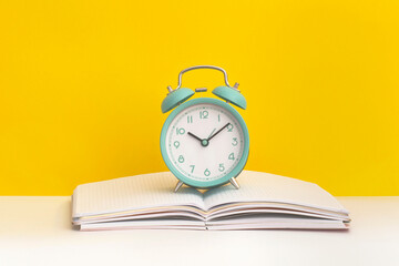 Notebook and alarm clock on yellow background. Top view. Flat lay. Back to school concept.