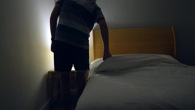 Man prepares to go to bed and sleep. Person lays down in bed and turns off night stand besides bed