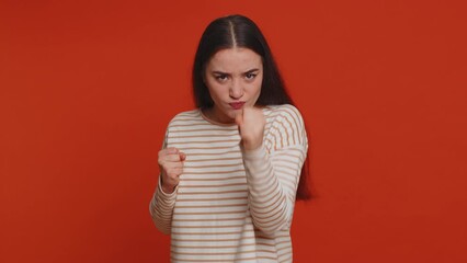 Angry aggressive pretty woman trying to fight at camera, shaking fist, boxing with expression, punishment, disappointment, rage, quarrel. Young adult girl isolated alone on red studio wall background