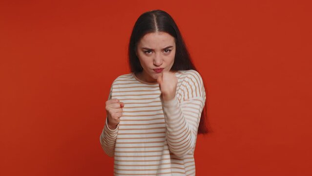 Angry aggressive pretty woman trying to fight at camera, shaking fist, boxing with expression, punishment, disappointment, rage, quarrel. Young adult girl isolated alone on red studio wall background