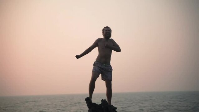 A guy on a rock against the backdrop of sunset and beats rumi on the chest.
