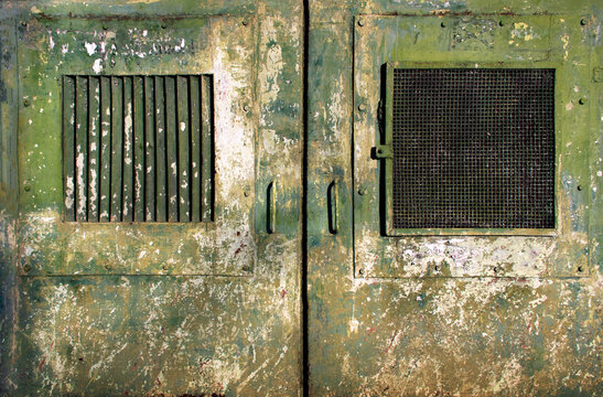rusty weathered and dirty metal doors with windows of a military bunker or prison with chipped khaki green- textured surface for dystopian cyber punk army in a world war scenario wallpaper background