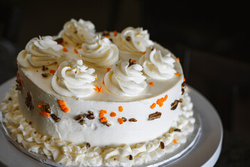 Obraz na płótnie Canvas A homemade gourmet carrot cake with decorative white frosting, colored sprinkles and walnuts on a white cake stand