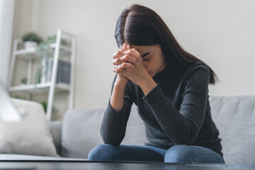 Unhappy anxiety young Asian woman covering her face with pillow on the cough in the living room at home.