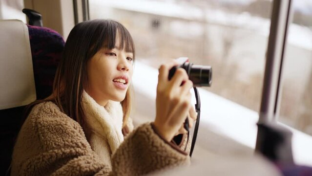Young Asian woman using digital camera taking picture of beautiful view out of the window during travel on train at sunset. Attractive girl travel Japan on railroad transportation on winter vacation.