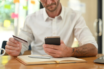 Cropped shot of man hand holding credit card shopping online, making payment for purchase on mobile phone