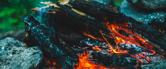 Vivid smoldered firewoods burned in fire close-up. Atmospheric warm background with orange flame of...