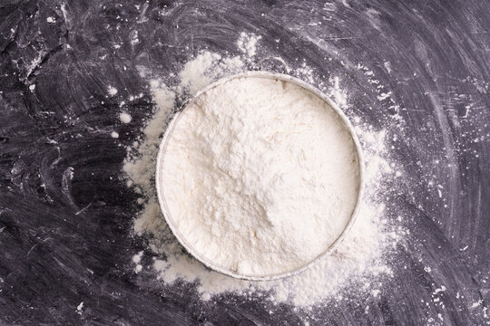 Flour in a bowl and wheat flour on table, black background In a rustic kitchen, top view