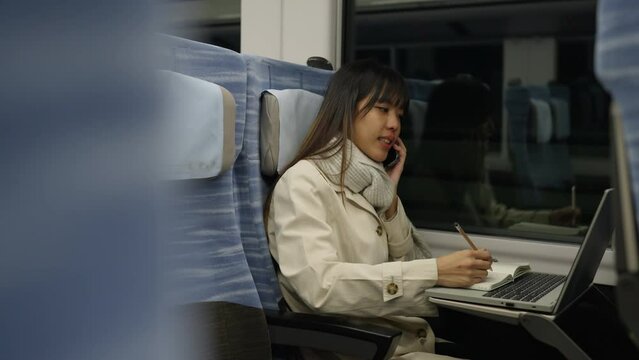 Asian businesswoman working on laptop computer and talking corporate business on cellphone during travel on railway transportation. Young woman freelance working on train. work from anywhere concept.