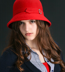Headshot of beautiful young woman with long brunette hair in vintage red cloche hat and preppy outift looking at camera - 575228965