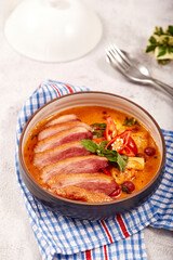 Red curry with roasted duck placed on a blue tablecloth, this food contains such as red curry paste, chili, tomato and pineapple.