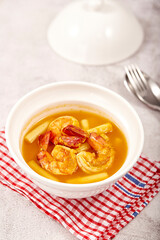 Sour soup with lotus stem and shrimps in a white bowl on table. local food of Thailand.