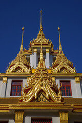 Fototapeta na wymiar Looking up at the detail of the golden spires against blue sky of Loha Prasat, Iron castle or iron monestary officially called Wat Ratchanatdaram Worawihan in Bangkok, Thailand.