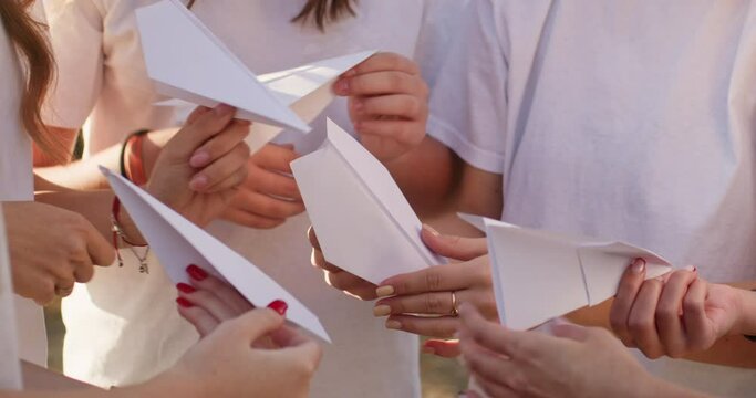 Teenage girls hold paper airplanes and prepares to launch in city park. Group of teenagers learns to make nice paper airplane