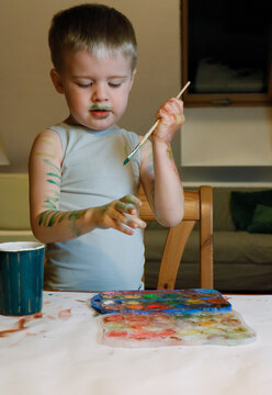 The boy is engaged in creativity - he paints his hands with paint