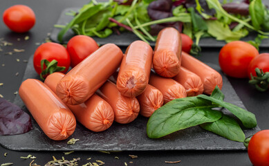 Tasty boiled sausages with cherry tomato and green leaves for salad on the black table. Cooking food. - 575242159