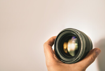 Modern digital camera lens in hand close up over light background. Banner image with a copy space of a lens in hand. - obrazy, fototapety, plakaty