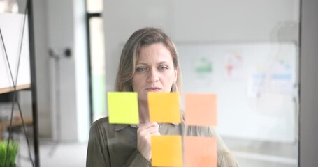 Thoughtful businesswoman leader in modern university office looks at sticky notes about project strategy