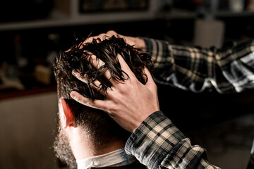 close-up of hands of the master apply protective oil to the hair on male head