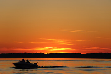 Silhouette of two fisherman on the boat. Beautiful sunset on the background.