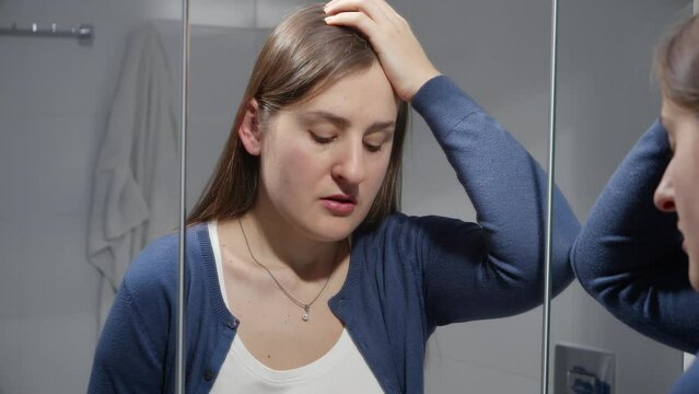 Upset depressed woman standing in bathroom and leaning on mirror. Concept of depression, stress, mental illness and problems, loneliness and frustration