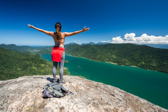 Young woman on mountain with arms outstretched, Saco do Mamangua, Paraty, Costa Verde, Brazil
