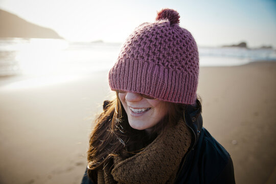 A woman wears a toque over her glasses while walking the beach.