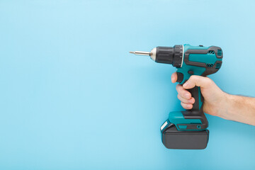 Young adult man hand holding and showing dark black green professional battery screwdriver on light blue wall background. Pastel color. Closeup. Tool for repair work. Side view. Empty place for text.