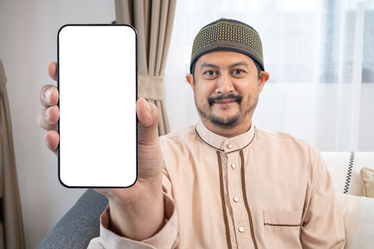 Smiling young Asian Muslim man showing mobile phone with white screen.