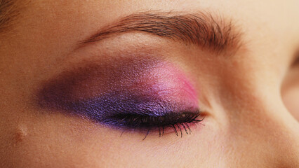 Close-up of a woman's eye with bright shiny makeup.  The blinking eye of a girl in profile. Pink-purple sequined fashion makeup.  Beauty fashion makeup.