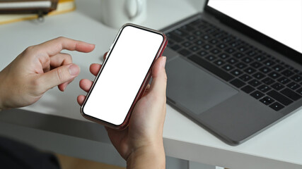 Man holding smartphone white screen while sitting in front of laptop at workplace. Blank screen for advertise webpage or text