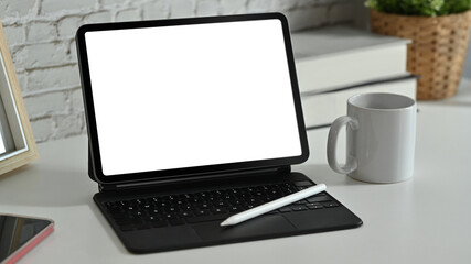 Digital tablet with wireless keyboard, coffee cup and supplies on white working desk. Blank screen for advertise webpage or text