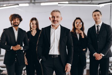 Confident company ceo standing in front of employees. Smiling coworkers posing with their boss in office. International business team