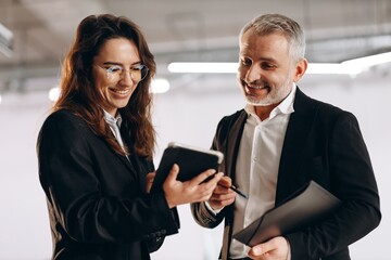 Smiling woman showing digital tablet to her boss. Indoor shot of happy businesspeople with digital device in office. Business technologies