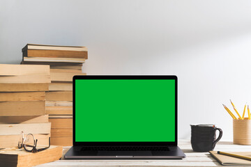 Chroma key green screen laptop on table with pile of books on the table