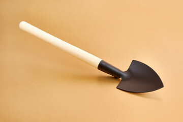A small metal shovel with a wooden handle on a golden background.