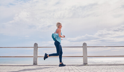 Senior woman running outdoor at beach promenade, sky mockup and energy for health, wellness and...