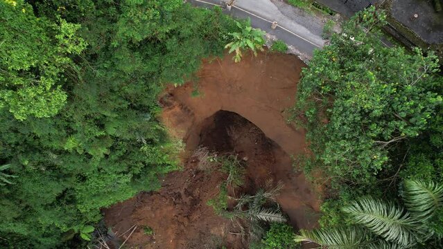 Dangerous collapse of steep slope destroyed half road, aerial view of landslide at central Bali. Heavy rains during rainy season and unstable soil caused mass movement of land and created danger