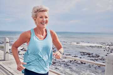 Senior woman, fitness and running at beach promenade, sky mockup and energy of health, wellness and workout. Elderly female, exercise and runner at ocean for happy sports, cardio training or marathon