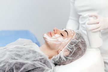 Cosmetologist is applying cream with anesthesia on patient's face skin before biorevitalization...