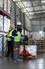 Worker in auto parts warehouse use a handcart to work to bring the box of auto parts into the storage shelf of the warehouse waiting for delivery to the car assembly line