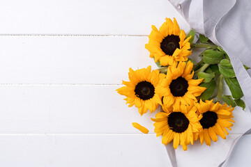 fresh sunflowers with leaves on stalk in shopping bag on wooden background. Flat lay, top view, copy space.