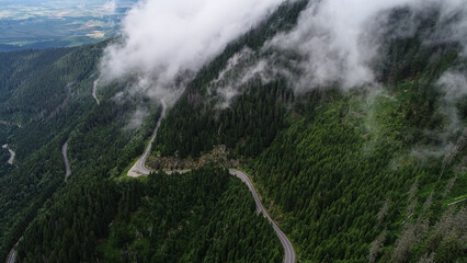 Amazing roads of the world. Aerial view over Transfagarasan landmark road of Romania, waving through the landscape of Fagaras Mountains in a cloudy day with fog coming out of the forest.