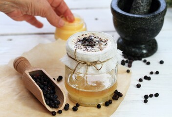 Alternative medicine, filtering juniper  ointment. Medicinal cream from dried common juniper berries, lat. Juniperus communis, good for joints. White wooden table, focus on running ointment.